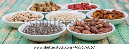 Super food tiger nuts, mulberry berries, cacao beans, goji berries, quinoa seeds, golden berry, chia seed in white bowls over wooden background