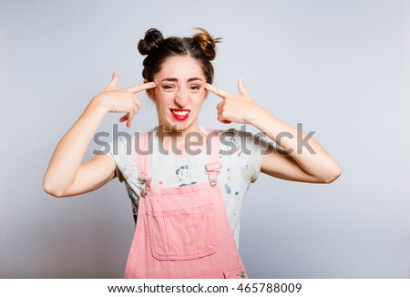 Bright young woman points a finger at the temple, dressed in a pink overalls, isolated on white background