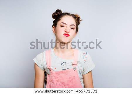 Bright young woman showing disgust, dressed in a pink overalls, isolated on white background