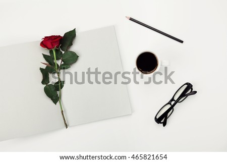 Womens working space with cup of coffee, pencil, empty notebook, glasses and rose flower on white table overhead view. Flat lay styling.
