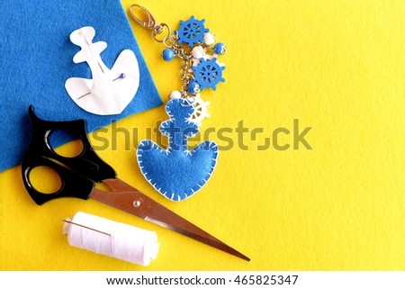 Felt anchor keychain, scissors, thread, pins, paper pattern, blue felt piece on yellow background with empty place for text at right side. Handicrafts concept. Home made key chain for car or bag 