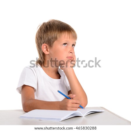 Cute young boy doing his homework at home sitting at the table looking to heaven with a thoughtful expression  isolated on white background