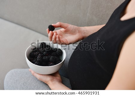 Young pregnant woman holding a plate of blackberries in her hands showing a healthy approach to the pregnancy