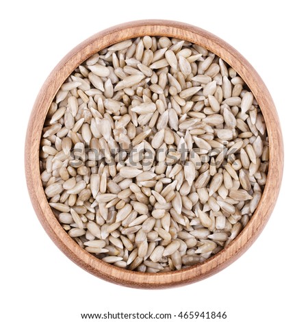 Sunflower seeds in a wooden bowl on white background. Shelled edible raw sunflowerseeds of Helianthus annuus, botanically it is a cypsela. Isolated close up macro photo from above.