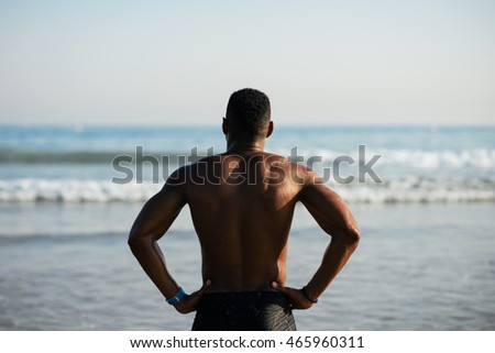 Back view of black fit sportsman looking the sea for motivation before swimming. Male swimmer ready for outdoor training into the ocean.