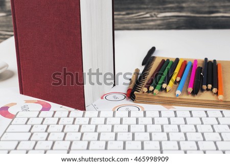 Closeup of workplace with computer keyboard, business report, vinous book and colorful supplies on wooden background