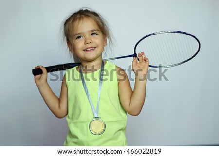 Pretty small girl in yellow t-shirt with badminton racquet and gold medal on her neck over white background, indoor portrait, sport and health concept Royalty-Free Stock Photo #466022819