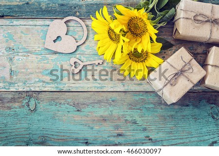 Background with yellow sunflowers, gift boxes, heart-lock and key on old wooden boards with peeling paint. Space for text.