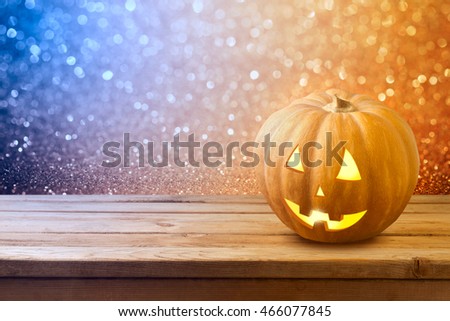 Halloween background with pumpkin jack lantern on wooden table over bokeh lights 