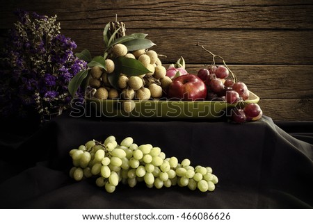 still life fruit include grape ,longan, dragon fruit, apple and dried flower on black cloth.  Adjustment  beautiful color image sepia style. 