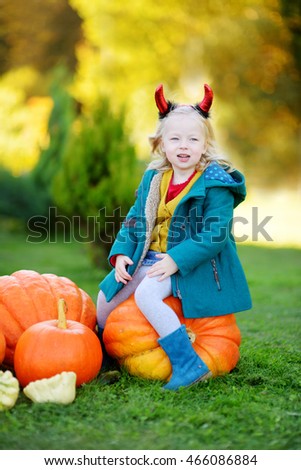 Adorable little girl wearing halloween costume having fun on a pumpkin patch on beautiful autumn day