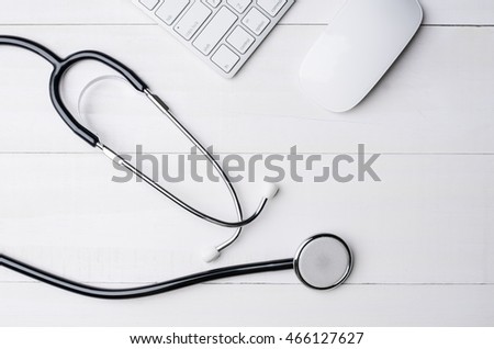 Top view of white wooden working table with computer keyboard, computer mouse and stethoscope. View from above with copy space.