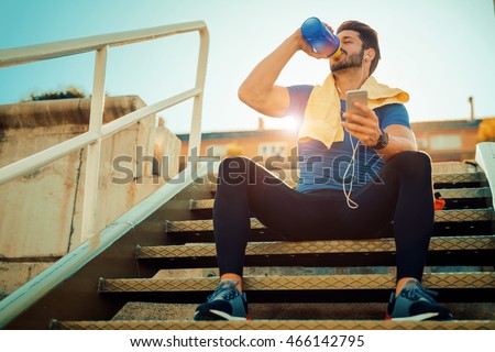Tired fitness man sweating taking a break listening to music on phone after difficult training.Fitness,sport,training and lifestyle concept. Royalty-Free Stock Photo #466142795