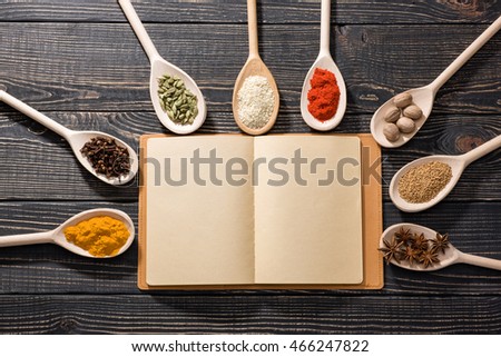 Colorful aromatic spices and open recipe book, on dark wooden background, view from the top