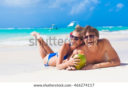 portrait of young couple lying on a tropical beach in Barbados and drinking a coconut cocktail