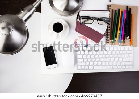 Top view of wooden office desktop with blank smartphone, computer mouse, keyboard, colorful supplies, glasses, book, coffee cup, table lamp and other items. Close up, Mock up