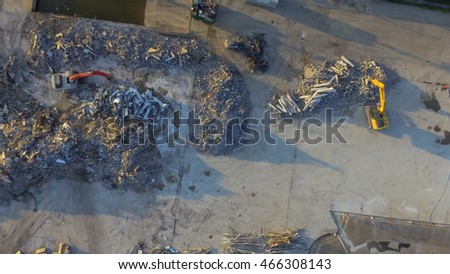 Aerial view construction site with rubble and scrap remaining after derelict building demolition. Hydraulic backhoe bulldozer removes crumbling demolished debris, brick, stone and concrete for recycle
