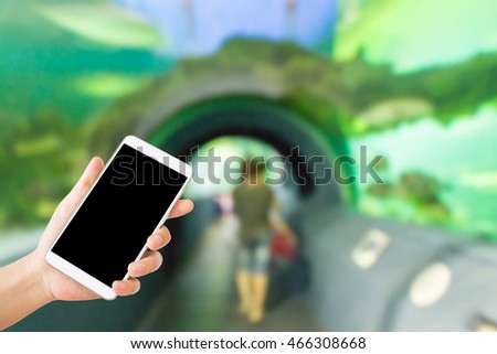 woman use mobile phone and blurred image of people in the aquarium tunnel