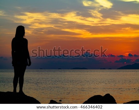 Silhouette of young woman standing on a rock with sunset.