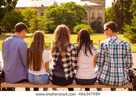 back view photo of five diverse students sitting on bench and study up