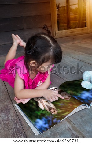 Closeup handsome asian girl smiling and reading picture album, lying on wooden floor with bright sunlight, outdoor at home. Children read and study, education concept.