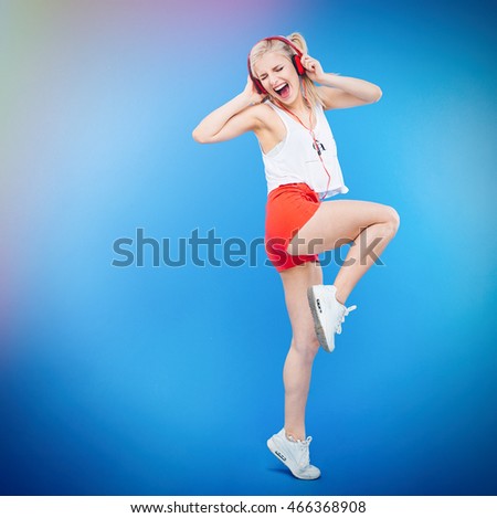 Full length portrait of a female teenager listening music in headphones and singing over blue background