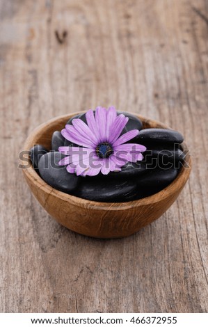 Pink flower with black stones in wooden bowl on old wood