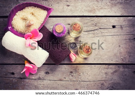 Wellness or spa  setting. Bottles with aroma oil, sea salt, towels  and  pink plumeria on vintage wooden background. Selective focus. Place for text. Toned image.