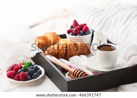 Morning breakfast in bed with cup of coffee, croissants, fresh berries and honey on wooden tray, selective focus