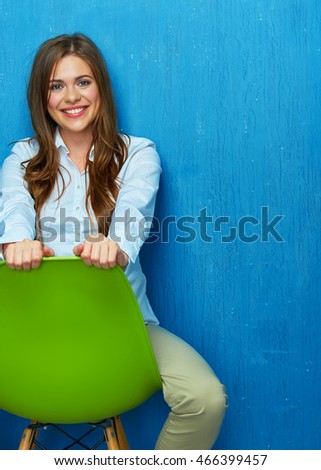 Beautiful young woman portrait sitting on chair. Blue wall background.