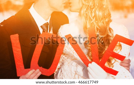 couple newlywed kissing with love red letters in the front winter snowy close up portrait