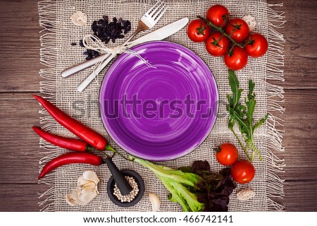 Fresh tomatoes, chili pepper and other spices and herbs around modern Turquoise plate in the center of wooden table and cloth napkin. Top view. Blank place for your text. Close-up.
