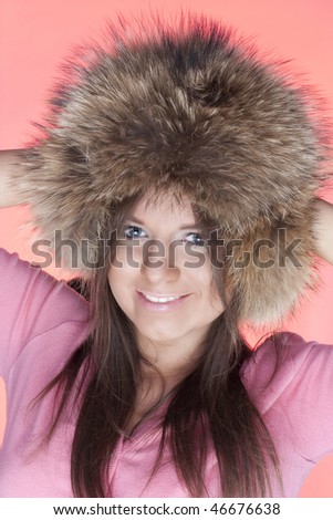 Portrait  of young girls in a fur cap on a pink background