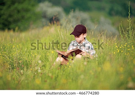 boy reads a book while sitting on the grass under a tree
