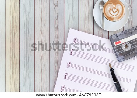 Sheet music, fountain pen, tape cassette and coffee latte on vintage wooden table, flat ray