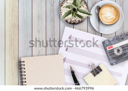 Sheet music, cactus, fountain pen, tape cassette and coffee latte on vintage wooden table, flat ray