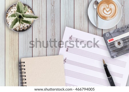 Sheet music, cactus, fountain pen, tape cassette and coffee latte on vintage wooden table, flat ray
