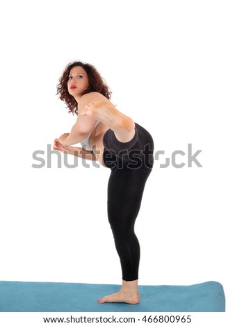 An exercising young woman in black pants standing on a blue mat,
kicking with her leg, isolated for white background.
