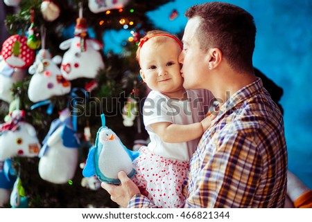 Brunette father in plaid shirt holds little smiling daughter in his hands
