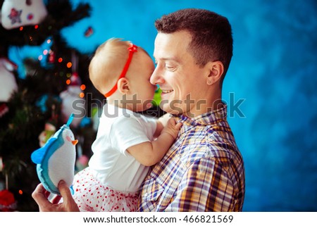 Smiling dad holds s little toy penguin while hugging his little daughter