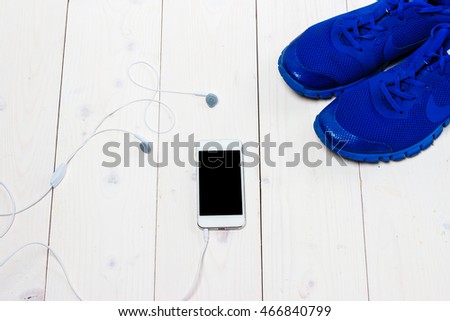Sneakers, earphones and phone on wooden background.