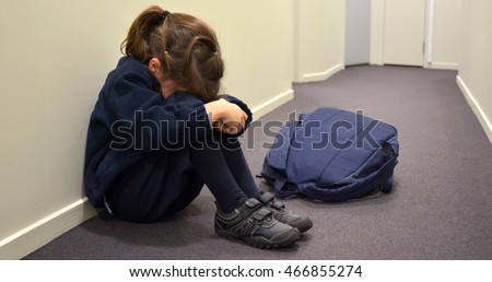 Portrait of one young elementary school girl (female age 5-6)  wearing school uniform and backpack sitting on a corridor floor covering face while crying.Bulling concept. Real people. Copy space Royalty-Free Stock Photo #466855274