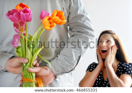 Surprised woman receiving tulip flowers from her lover that holding flowers boutique behind his back on Valentine's day. Couple relationship concept. Isolated on white background.Real people.Copy spac