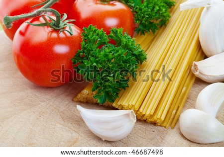 Pasta along with fresh vegetables on a wooden cutting board shallow depth of field