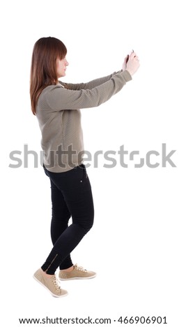 back view of standing young beautiful  woman  using a mobile phone. girl  watching. Rear view people collection.  backside view of person.  Isolated over white background. A girl in a gray jacket