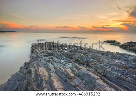 Beautiful sunrise view with long exposure shot to get moving clouds and creamy water effects over the rocks at the beach. Motion blur, soft focus due to slow shutter speed.