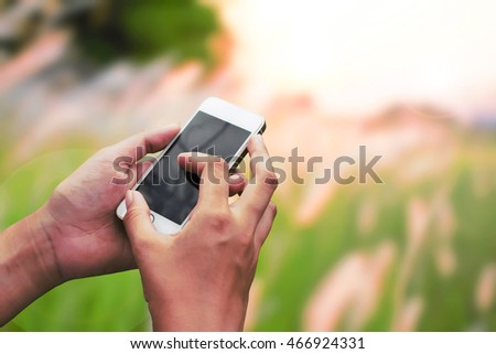 Hand hold and touch screen smart phone, on natural green blurred background.