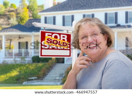 Senior Adult Woman in Front of Sold Home For Sale Real Estate Sign and Beautiful House.