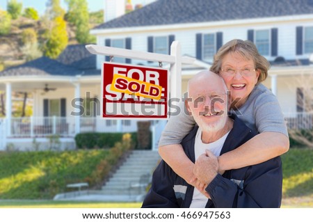 Senior Adult Couple in Front of Sold Home For Sale Real Estate Sign and Beautiful House.