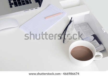 Cup of coffee, blank note with pencil and laptop on white table.